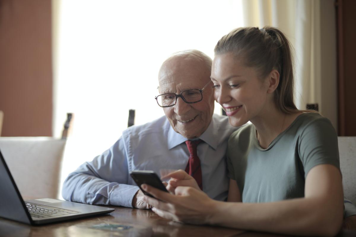 An elderly man and a younger woman using a smartphone together.